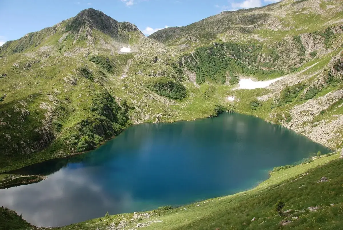Un incantevole lago ritorto, incastonato tra montagne verdi e rocciose, con chiazze di neve residua.