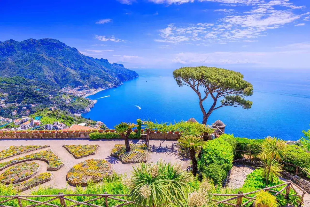 A stunning view of the Amalfi Coast, a perfect destination after arriving at Naples airport. Lush gardens overlook the sparkling blue sea and dramatic cliffs.