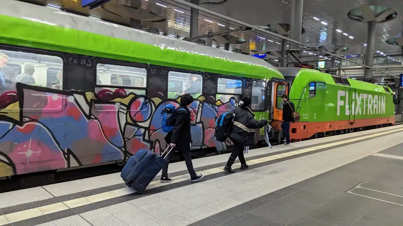Bunte Graffiti zieren den Flix Zug in Berlin. Reisende mit Gep&auml;ck warten auf dem Bahnsteig.