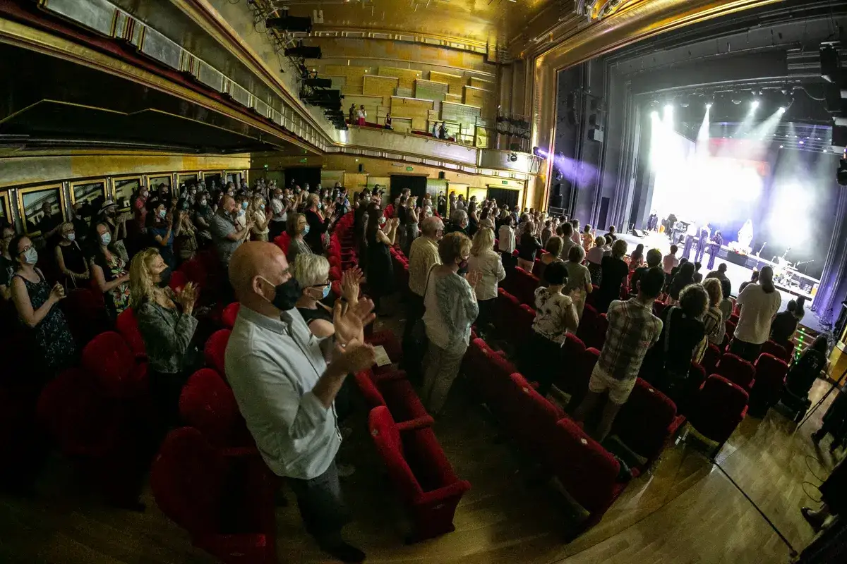 Widownia w Teatrze Capitol Poznań klaszcze po występie. Na scenie zespół muzyczny w świetle reflektorów.