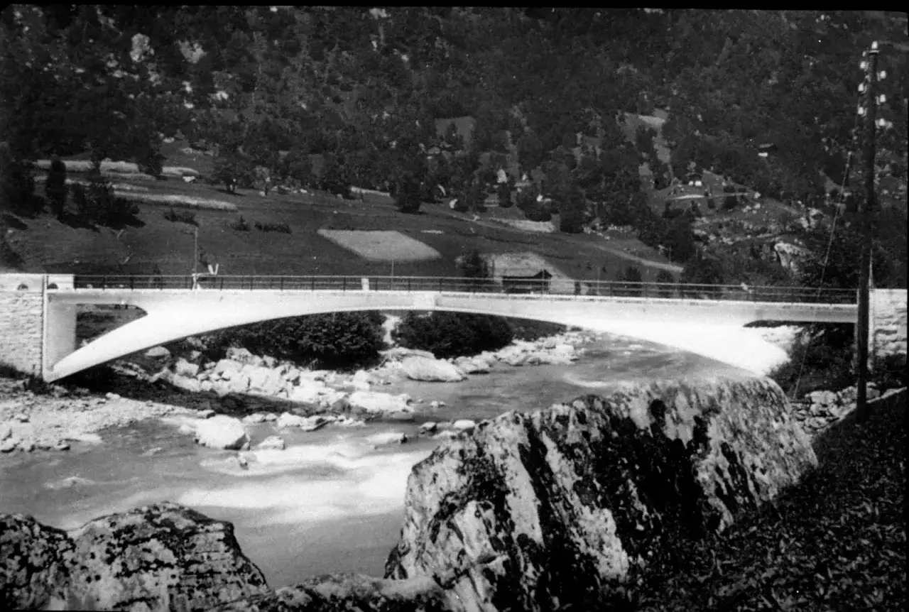 Puente de hormigón de **Robert Maillart** sobre un río rocoso, con colinas boscosas al fondo.