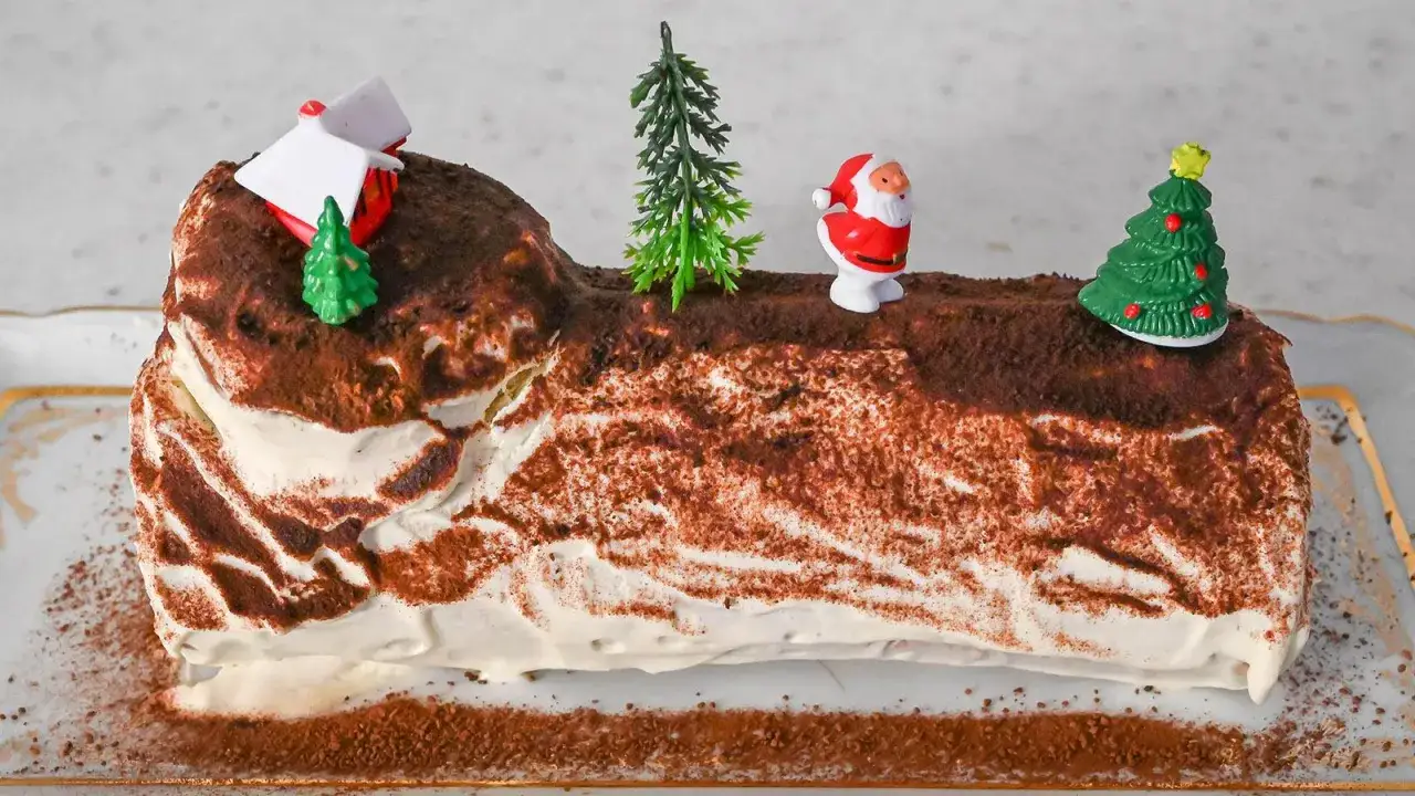 Ein festliches b&ucirc;che de no&euml;l rezept original, dekoriert mit Weihnachtsmann, B&auml;umen und einem Haus.