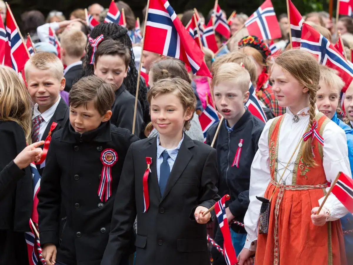 Dzieci w strojach narodowych i z flagami Norwegii. Ciekawe ciekawostki o Norwegii związane z tradycjami i świętowaniem.