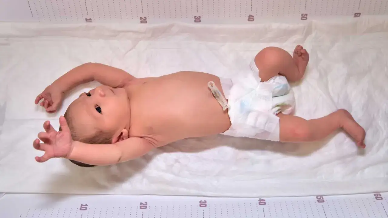 Neonato con pannolino e clip ombelicale, con le mani aperte e le gambe flesse, mostra i suoi riflessi neonatali su un telo con misurazioni.