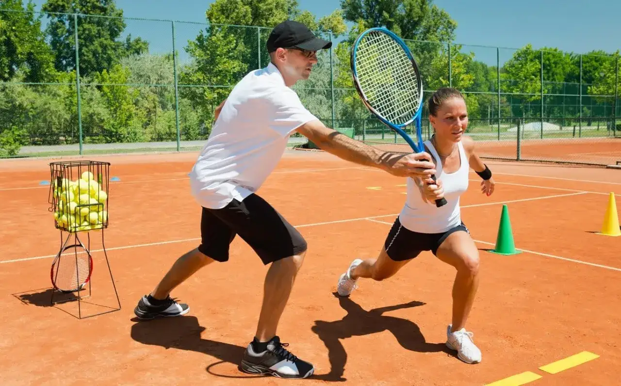 Trener pomaga kobiecie w przełamanie w tenisie, korygując jej chwyt rakiety na korcie.