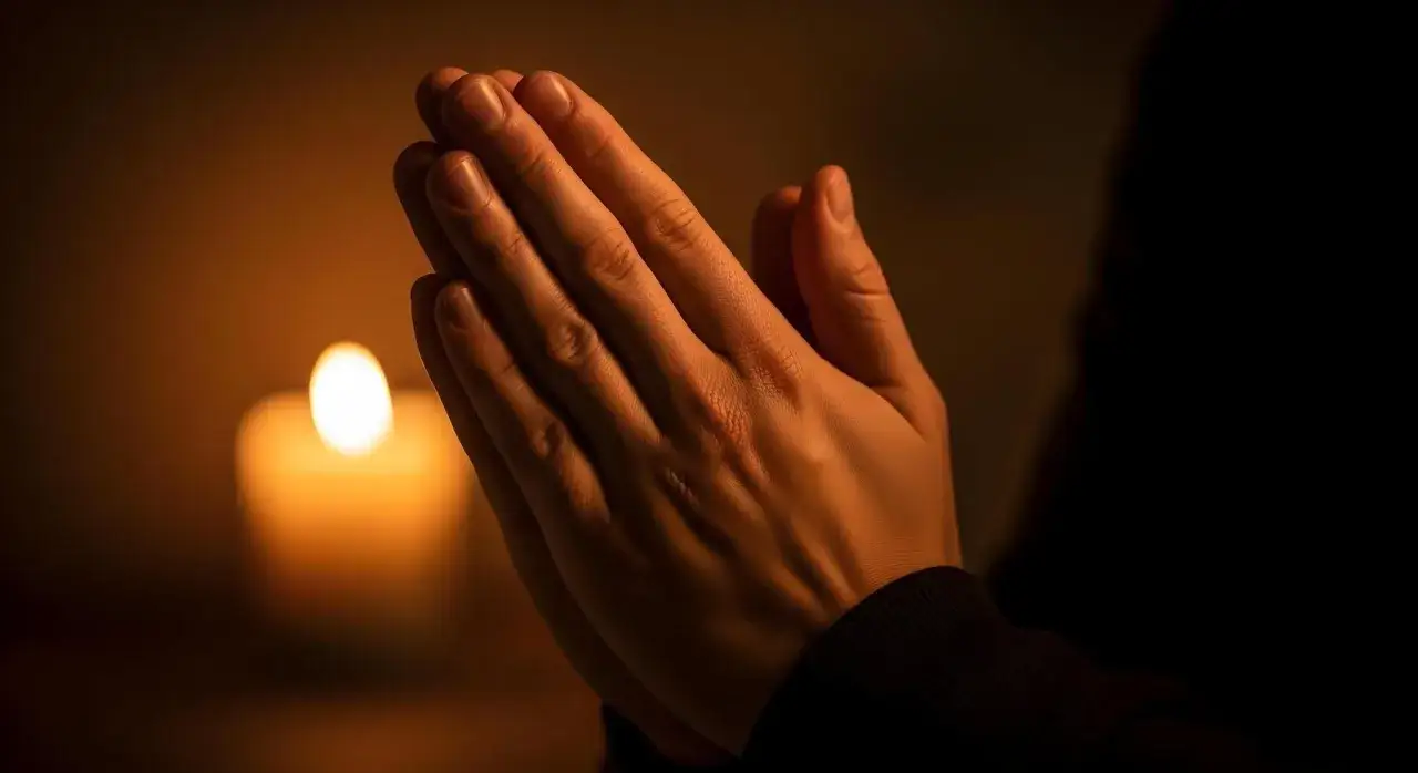Manos juntas en oraci&oacute;n ante una vela encendida, pidiendo que Deus nos aben&ccedil;oe e nos proteja.