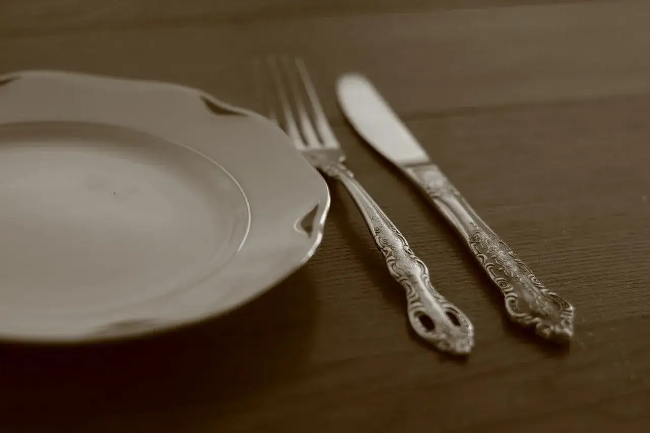 Une assiette blanche et une fourchette et un couteau en argenterie noircie, posés sur une table en bois.