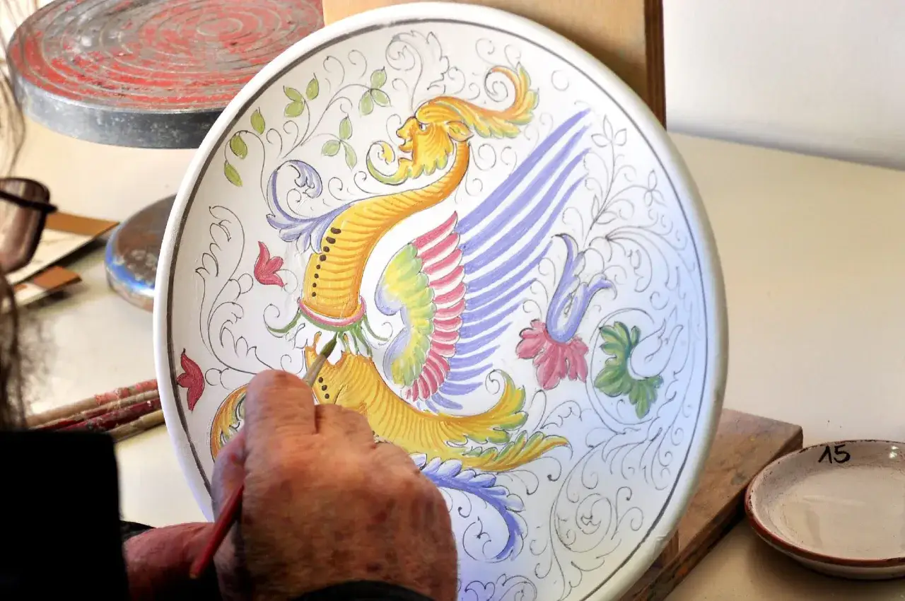 Un artista dipinge un grifone su un piatto di ceramica a Deruta. Un'opera d'arte da non perdere!