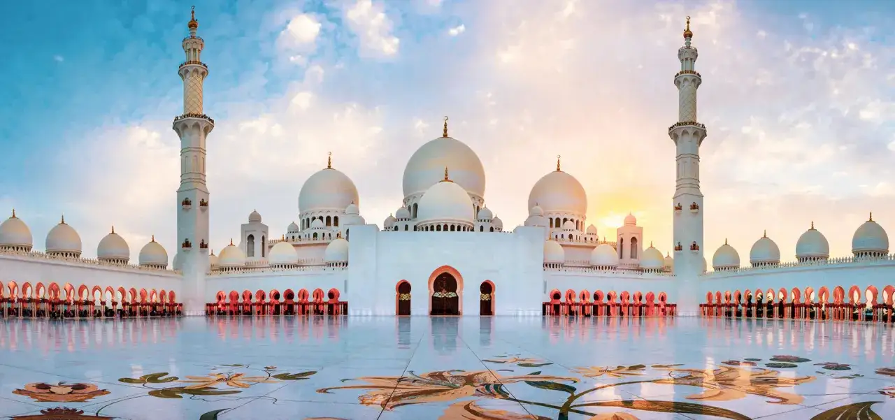 Wspaniały meczet w Abu Zabi, stolicy Emiratów Arabskich, o zachodzie słońca. Biała architektura lśni, a niebo maluje się ciepłymi barwami.