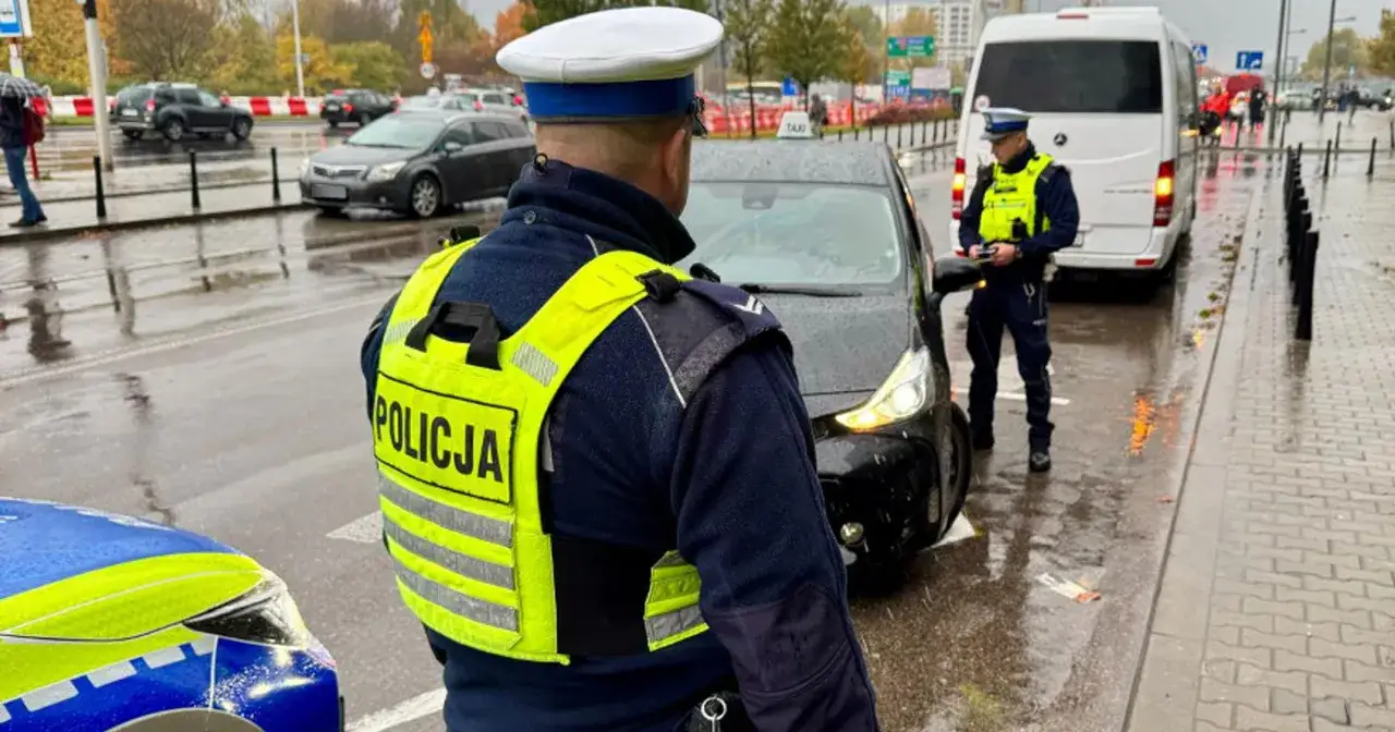 Policjanci w kamizelkach odblaskowych zatrzymali kierowcę. Na mokrej ulicy czeka go mandat.