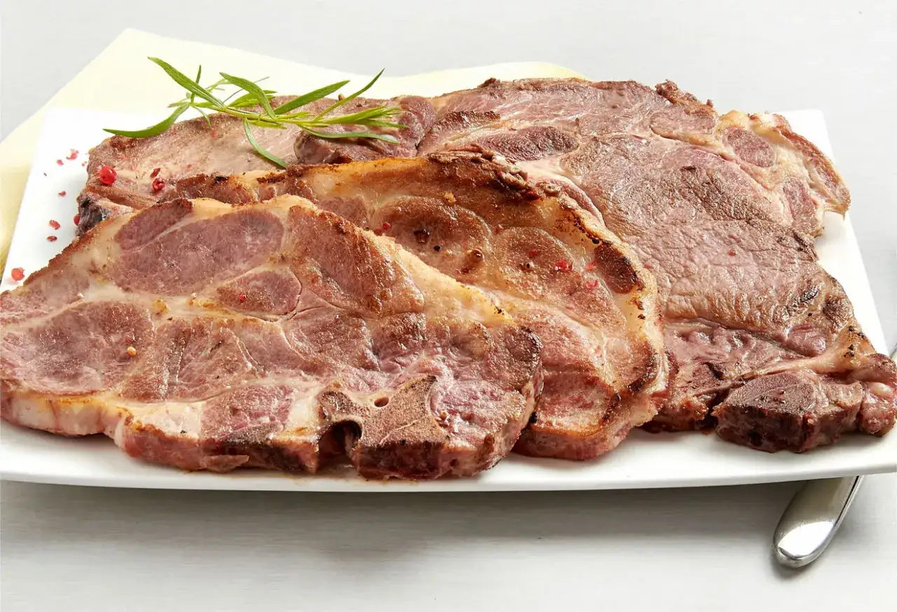 Plusieurs côtes de porc, viande blanche ou rouge, sont présentées sur une assiette blanche, garnies de romarin et de grains de poivre rose.