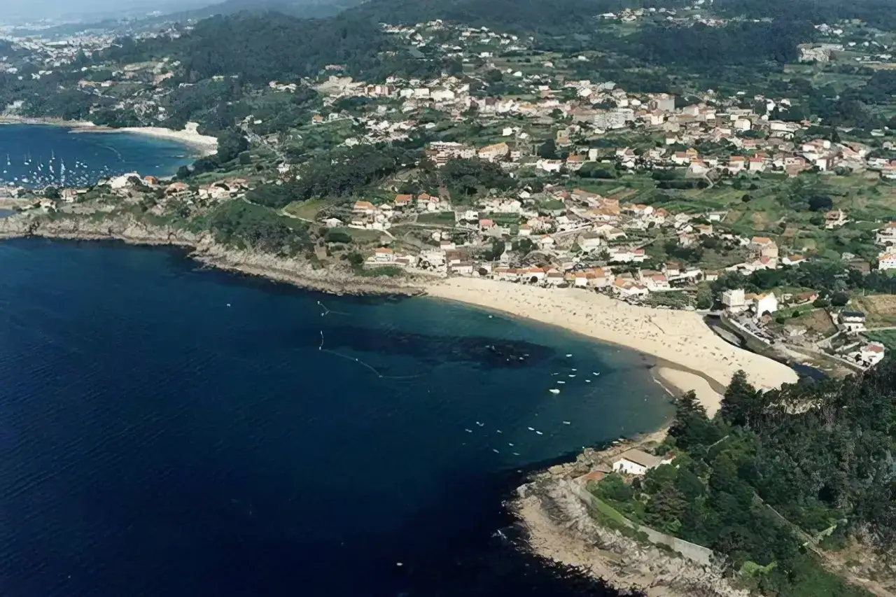 Vista aérea de la playa de Loira, con arena dorada, aguas azules y un pueblo costero en la ladera verde.