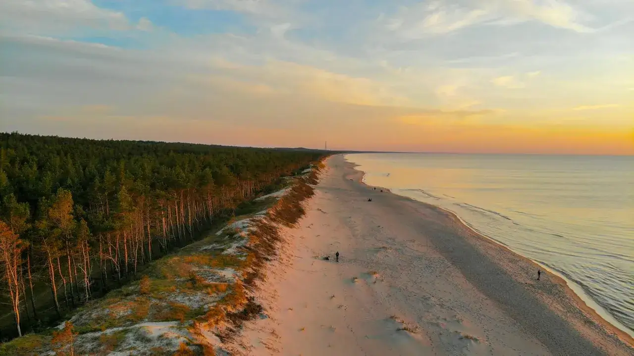 Zachód słońca nad polskim morzem. Piaskowa plaża, sosnowy las i spokojne fale. Idealne miejsce, gdzie nad morze w Polsce.