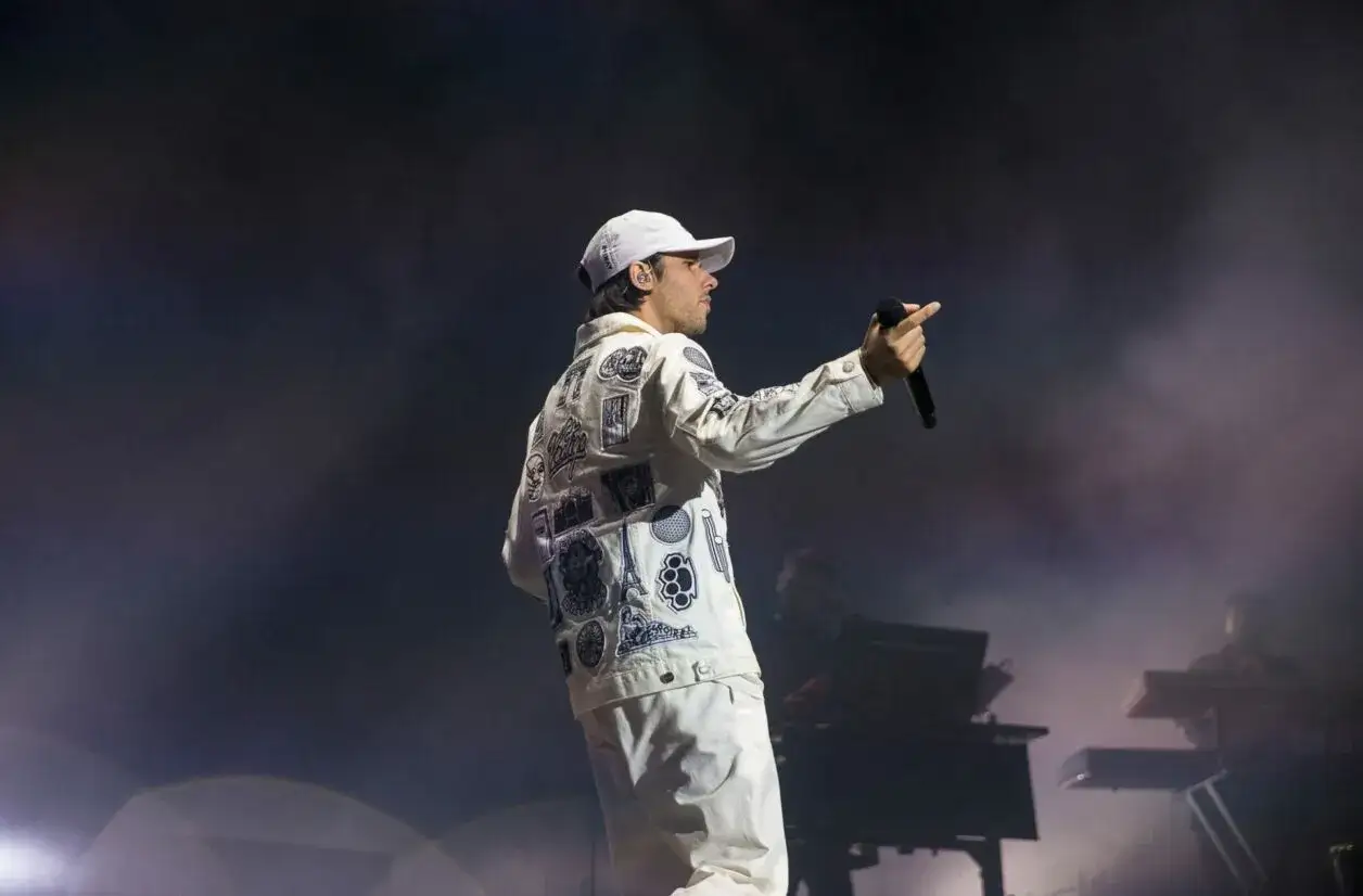 Un rappeur sur sc&egrave;ne, micro en main, porte une veste blanche orn&eacute;e de patchs. L'ambiance est &eacute;lectrique, typique d'un concert de rap.