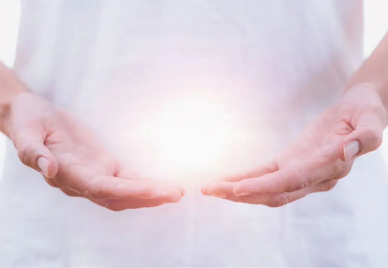 Manos abiertas sosteniendo una luz brillante, simbolizando la sanaci&oacute;n energ&eacute;tica y la esperanza.