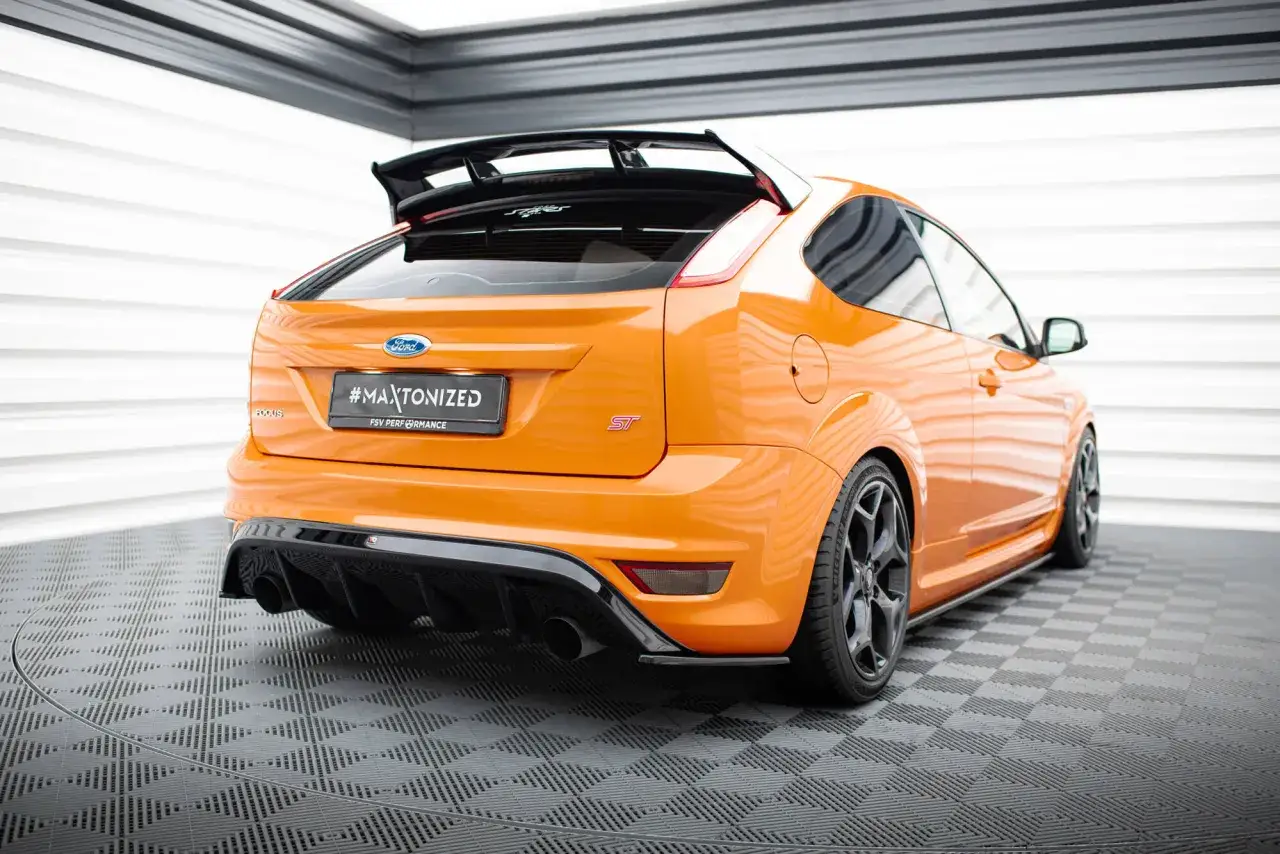 En orange Ford Focus Mk2 ST med en sportig bakdel och spoiler st&aring;r p&aring; ett rutm&ouml;nstrat golv.