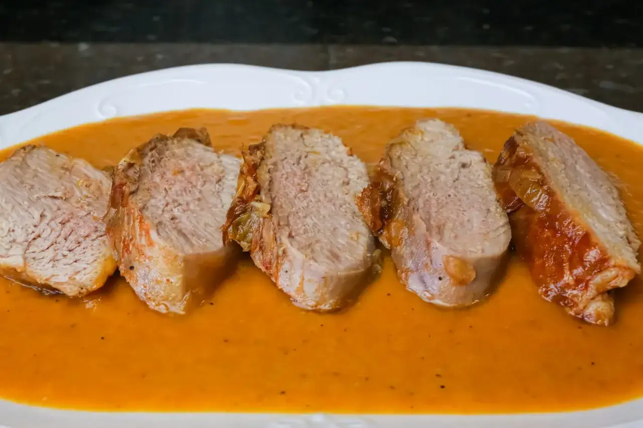 Cinco rodajas de jugosa carne al jerez, tierna y dorada, reposan en una cremosa salsa anaranjada sobre un plato blanco.