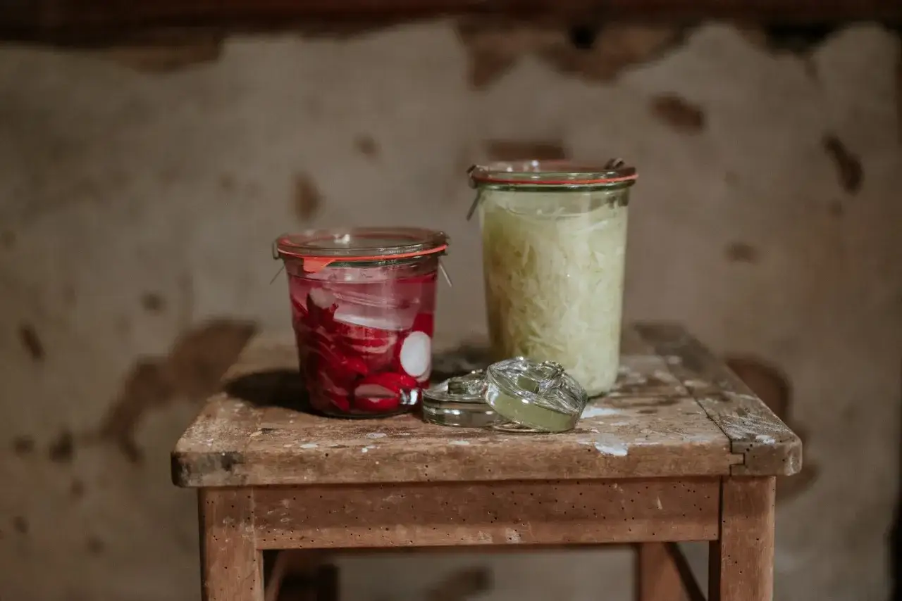 Zwei Gläser mit eingelegtem Gemüse, eines mit Radieschen, das andere mit Sauerkraut für ein einfaches Sauerkraut Rezept.