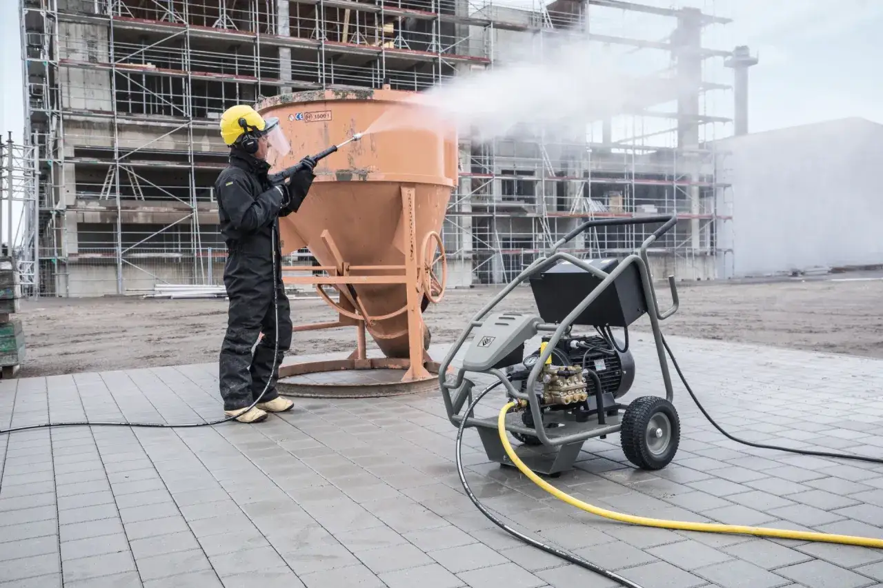 Mann reinigt mit einem Industrie Hochdruckreiniger einen Betonmischer auf einer Baustelle.