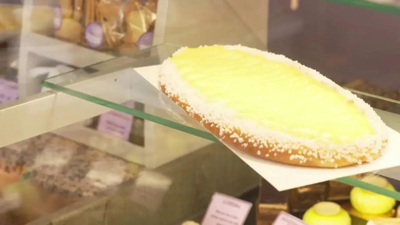 Une d&eacute;licieuse coca catalane, garnie de cr&egrave;me p&acirc;tissi&egrave;re jaune et de sucre perl&eacute;, attend dans une vitrine de p&acirc;tisserie.