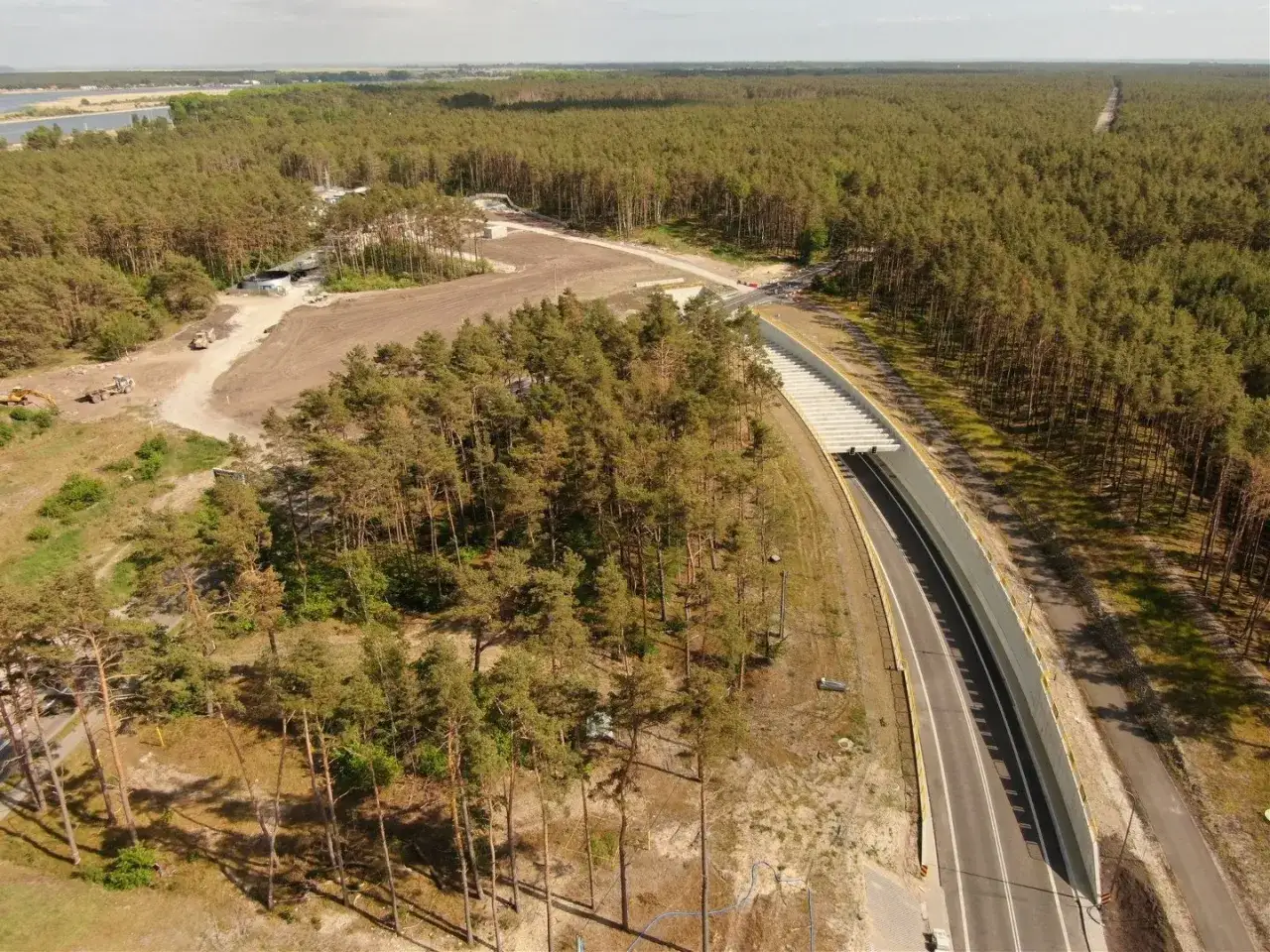 Budowa tunelu w Świnoujściu. Droga wjazdowa do tunelu otoczona lasem sosnowym, w oddali widać plac budowy.
