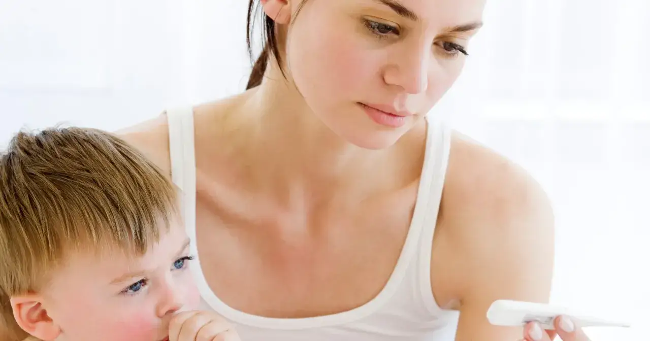 Zmartwiona mama sprawdza temperaturę chorego dziecka. Szuka informacji, jak zbić gorączkę u dziecka domowym sposobem.