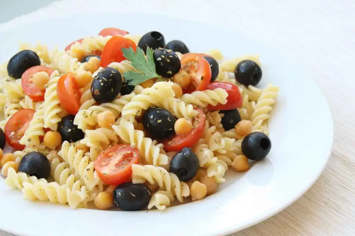 Un piatto invitante di pasta fredda con ceci, pomodorini e olive nere, condita con erbe aromatiche. Perfetta per un pasto estivo.