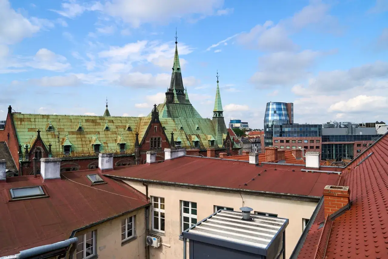 Widok na zabytkowy krajobraz miejski z zielonymi dachami i nowoczesnym budynkiem w tle.