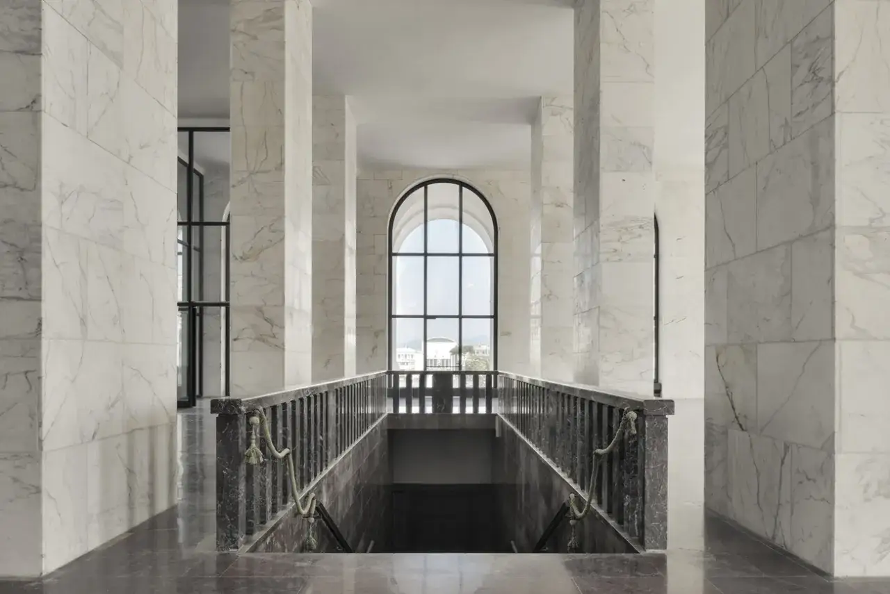 Interno del Palazzo della Civilt&agrave; Italiana: un corridoio con colonne in marmo bianco, una scalinata scura e una grande finestra ad arco che si affaccia sull'esterno.