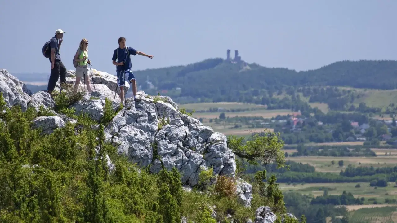 Turyści na skale wskazują drogę na szlakach Gór Świętokrzyskich. W oddali widać ruiny zamku.