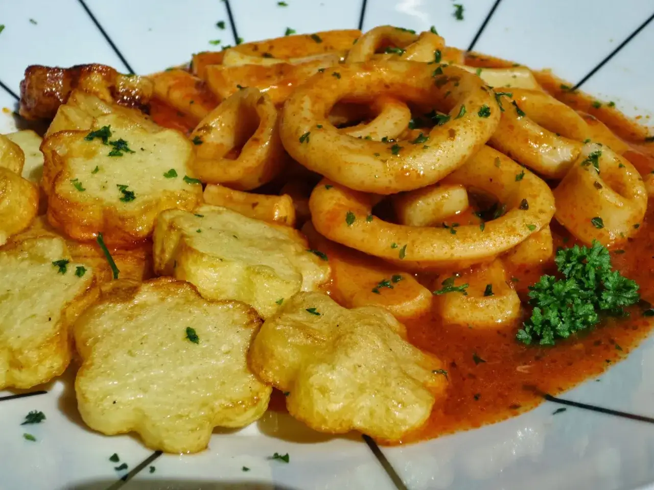 Calamares en salsa, con patatas fritas con forma de flor, todo espolvoreado con perejil fresco.