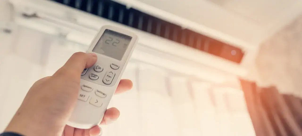 Mano ajustando el control remoto del aire acondicionado, mostrando la temperatura de 22 grados. ¿Qué potencia de aire acondicionado necesito para mi hogar?