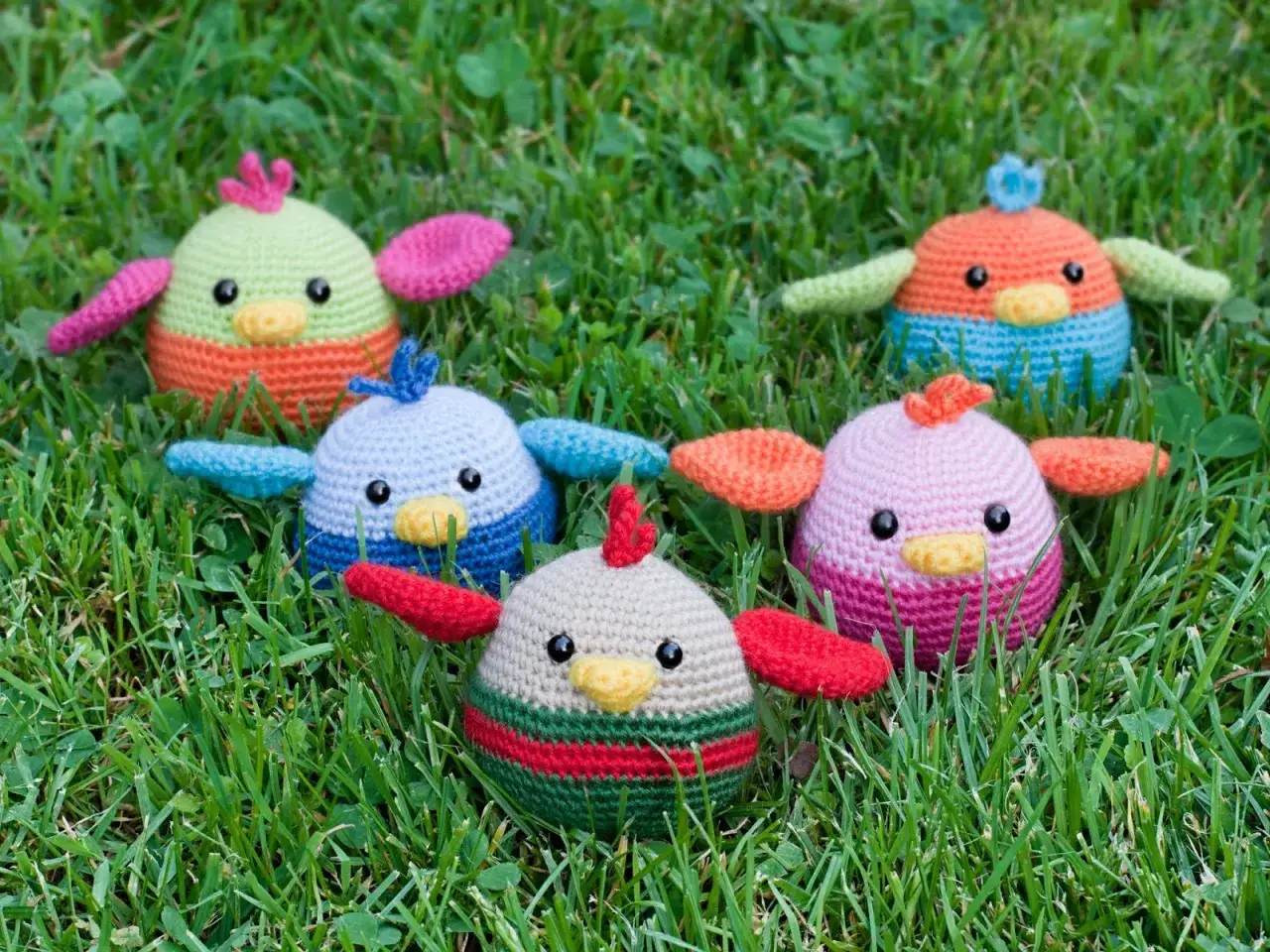 Cinco adorables pajaritos de ganchillo, con patrones coloridos, descansan sobre la hierba verde.