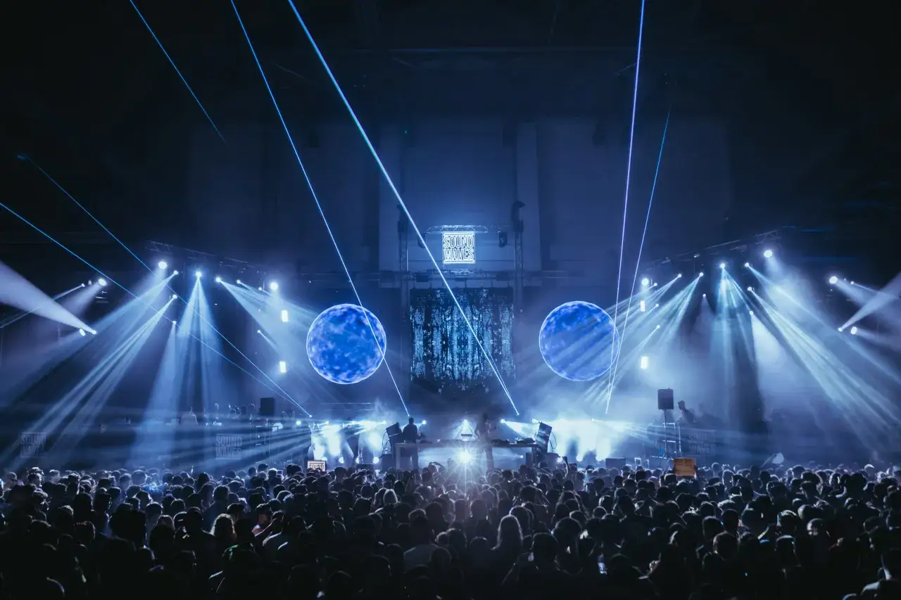 Eine riesige Menge tanzt im Takt von **techno beats**, w&auml;hrend blaue Laser und Scheinwerfer die B&uuml;hne in ein futuristisches Licht tauchen.