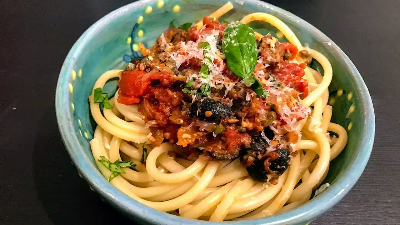En skål med pasta puttanesca, toppad med basilika och parmesan. Perfekt vin till pasta puttanesca.
