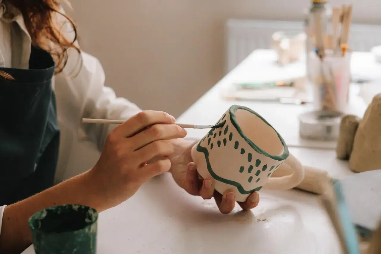 Tworzenie ceramicznego kubka na 9 rocznicę ślubu. Ręce artystki malują zielone wzory.