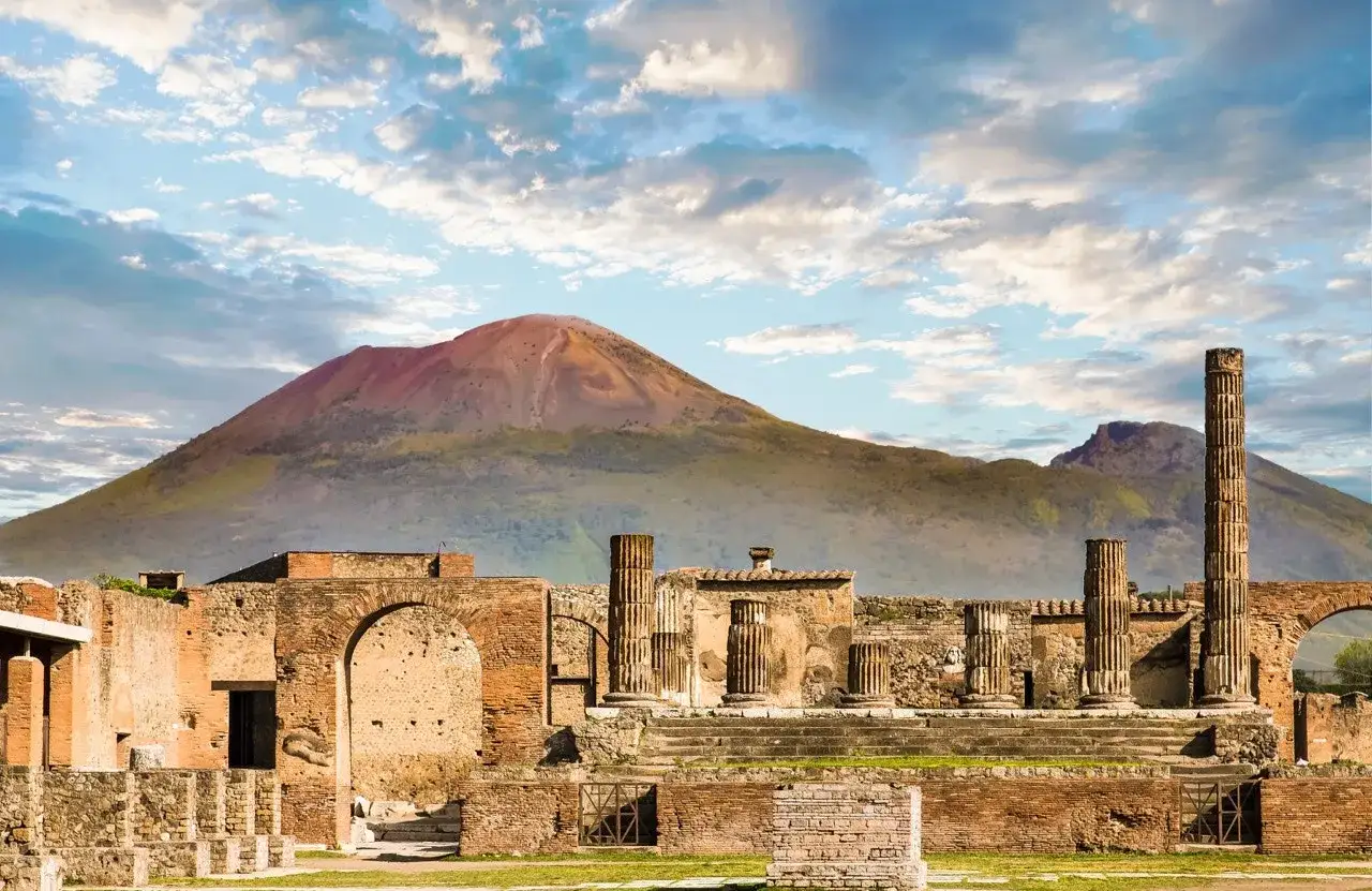 Ruinas de Pompeya y Herculano bajo el imponente Vesubio, con columnas y arcos de piedra que evocan la grandeza del pasado.
