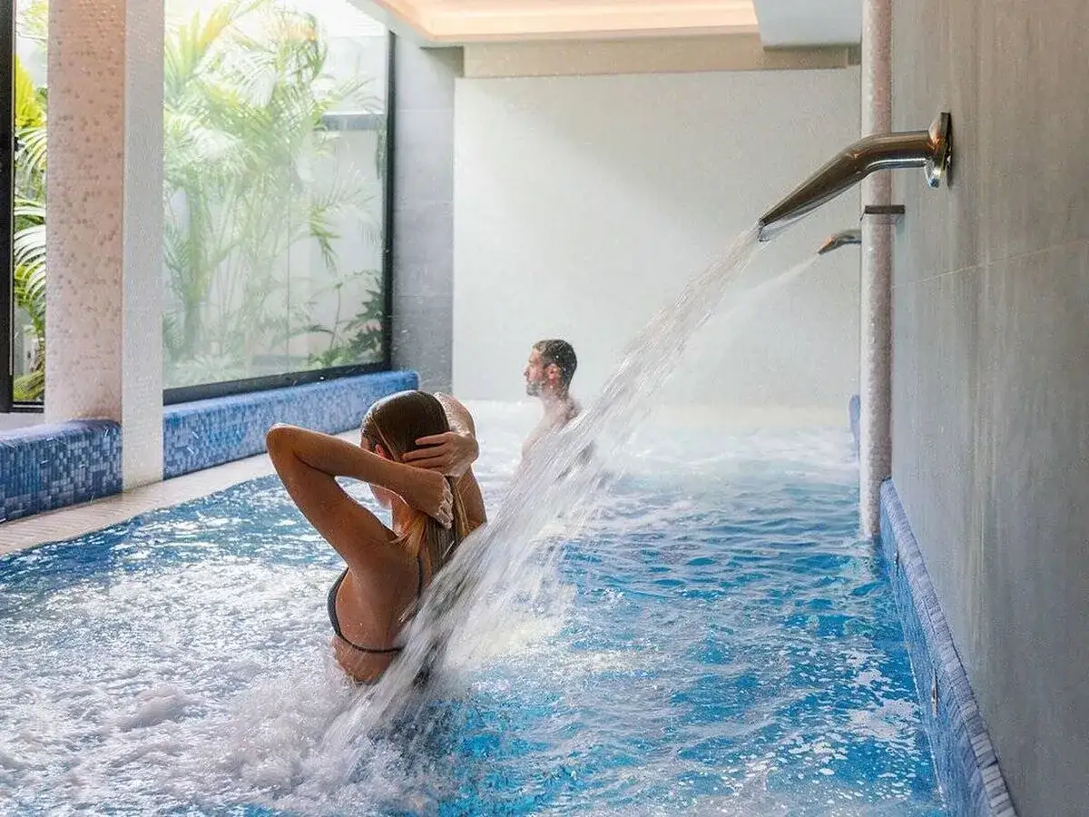 Pareja disfrutando de un chorro de agua en un centro de relax. El agua cae sobre la mujer mientras un hombre se relaja al fondo.