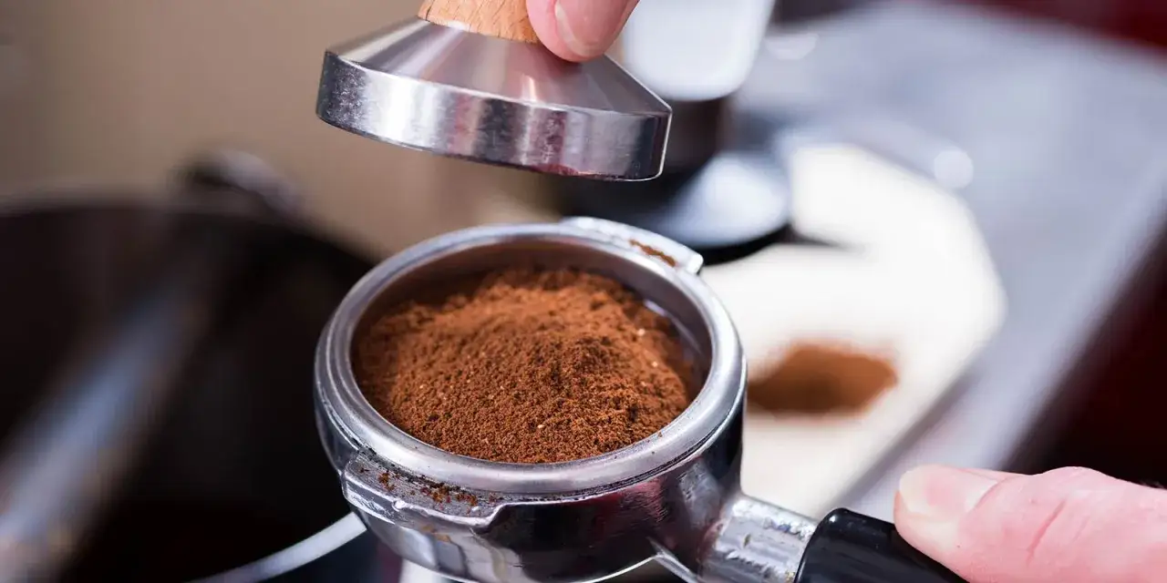 Fein gemahlener Kaffee in einem Siebträger, bereit für die Zubereitung mit einer Espressomaschine. Ein Tamper wird angesetzt.
