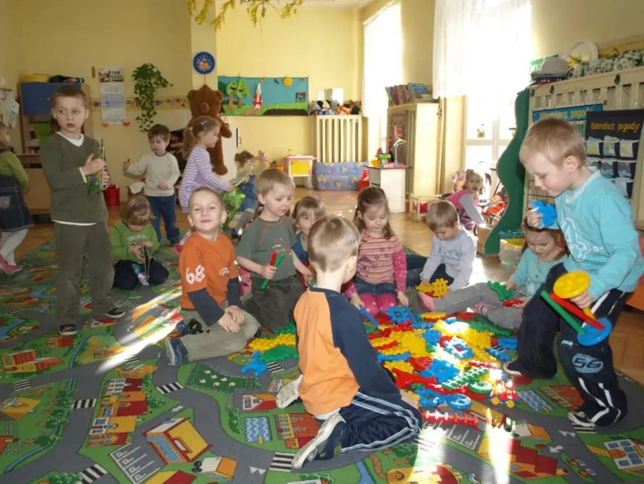 Dzieci bawią się klockami na dywanie w kształcie ulicy. To świetny dodatek do przedszkola, który rozwija kreatywność.