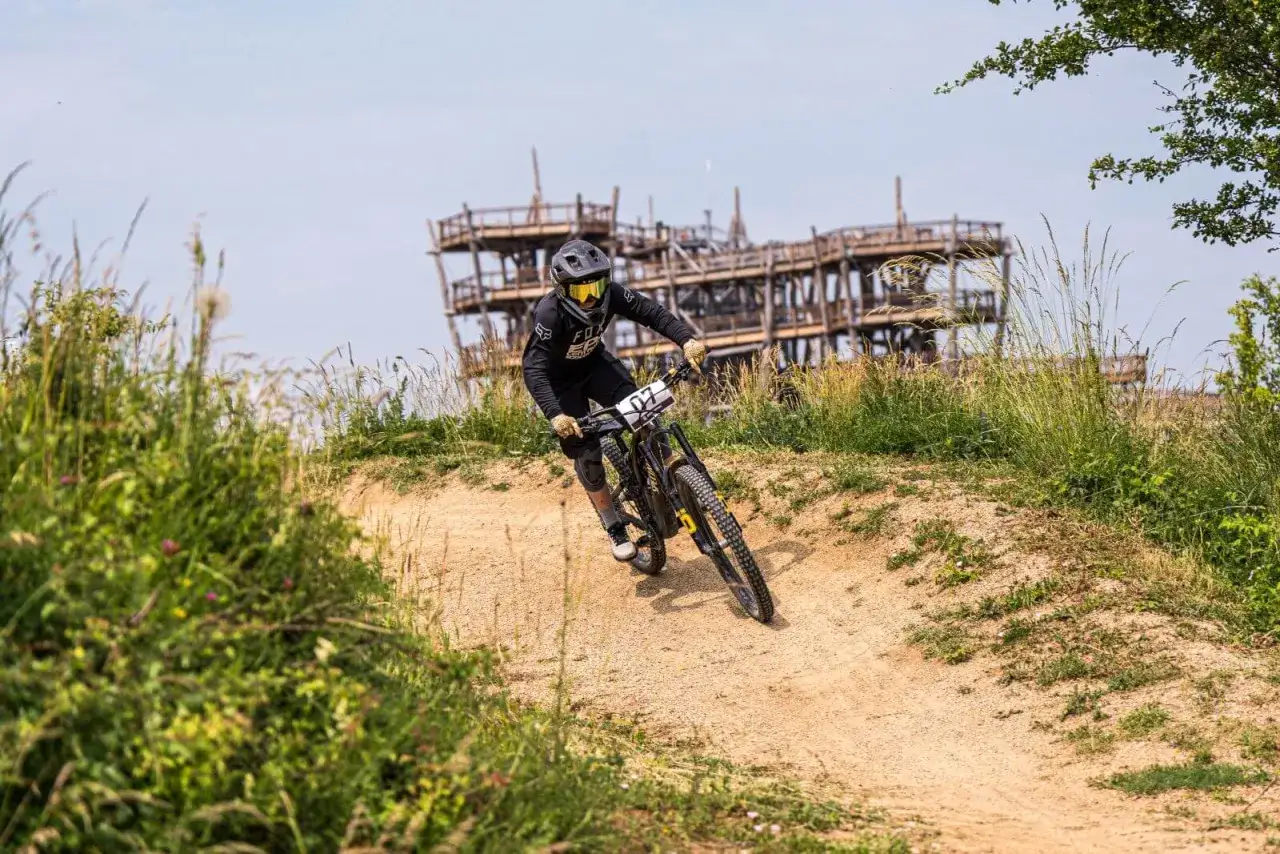 Rowerzysta zjeżdża po piaszczystym torze, testując jedne z najlepszych bike parków w Polsce. W tle drewniana konstrukcja.
