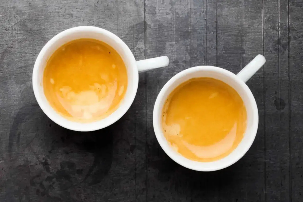 Zwei wei&szlig;e Tassen mit cremigem Kaffee shot auf dunklem Hintergrund.