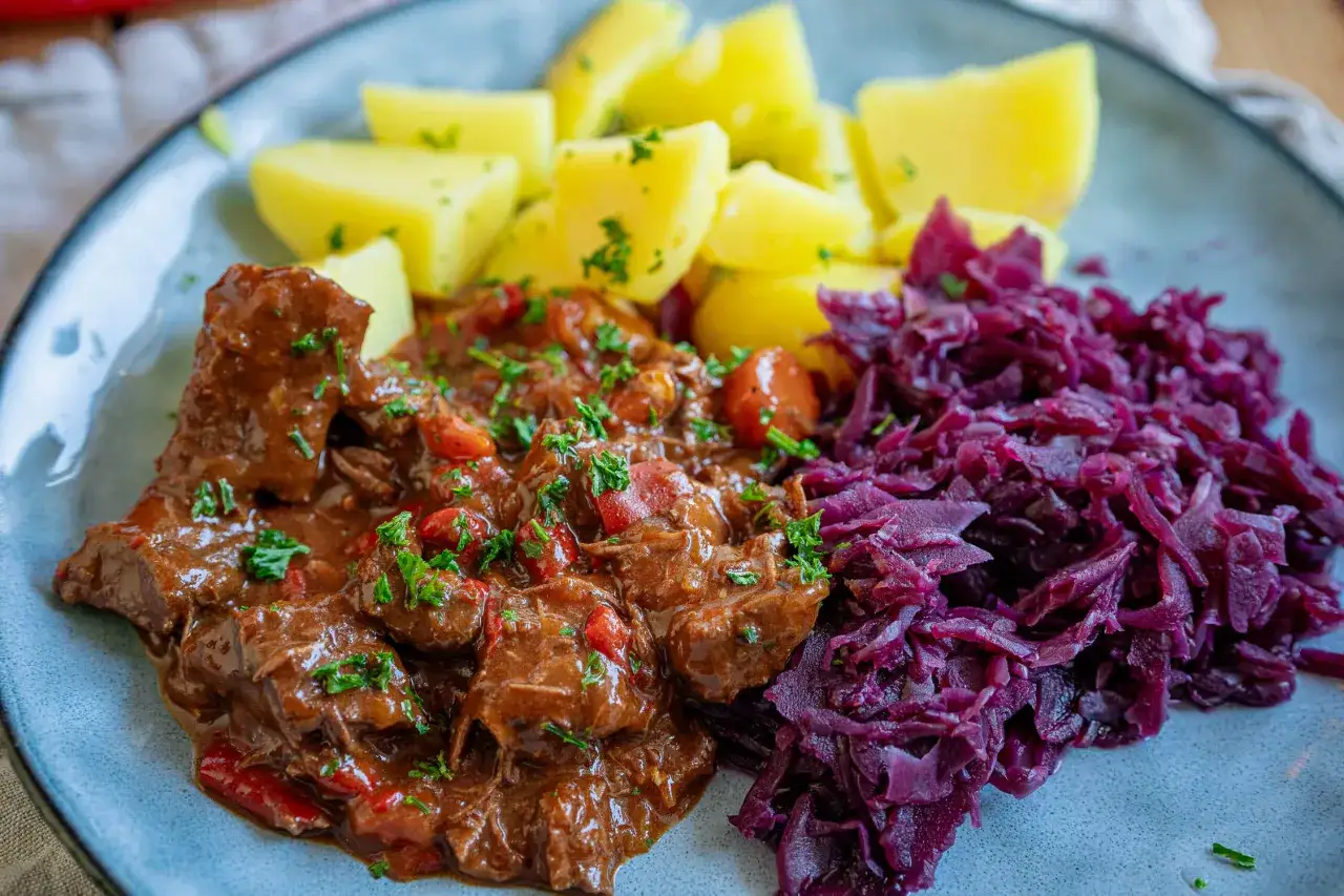 Herzhaftes Gulasch, ein typisches Gericht für schmorgerichte im ofen, serviert mit Salzkartoffeln und Rotkohl.