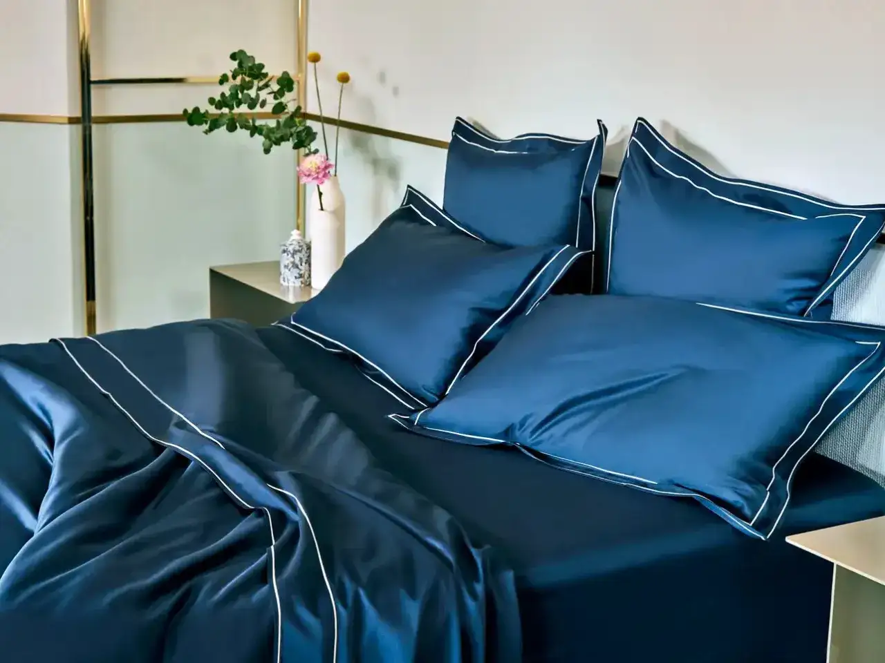 Letto matrimoniale con copriletto blu scuro e cuscini coordinati, rifiniti con bordi bianchi. Ideale per conoscere le misure copriletto matrimoniale.