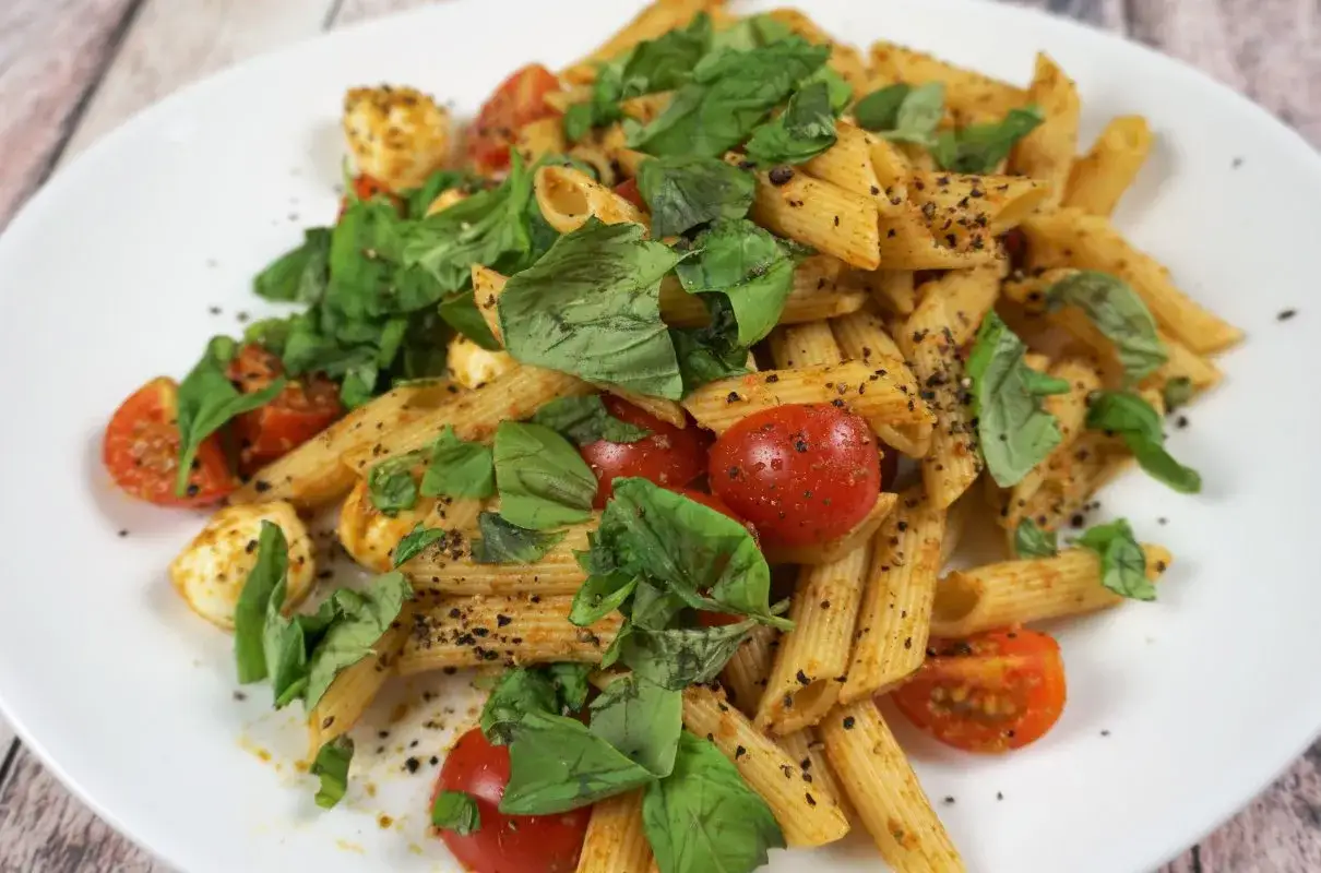 Penne z pomidorkami koktajlowymi, kulkami mozzarelli i świeżą bazylią, posypane pieprzem. Pyszne danie na szybki obiad.