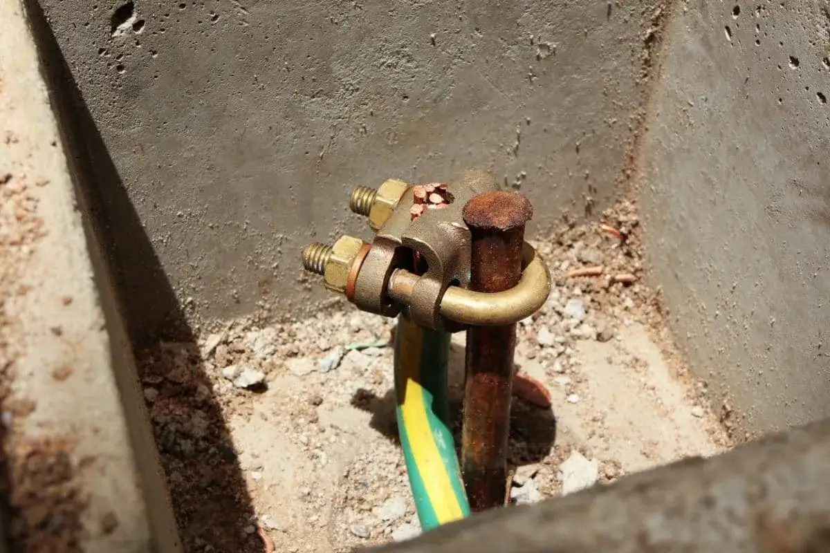 Gros plan sur un branchement prise de terre, avec une tige en cuivre rouill&eacute;e et un collier de serrage en laiton fixant un c&acirc;ble vert et jaune.
