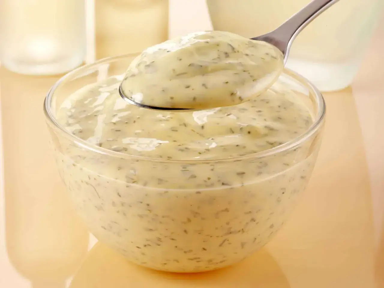Un cucchiaio raccoglie la cremosa salsa bernese da una ciotola di vetro, pronta per insaporire un piatto.