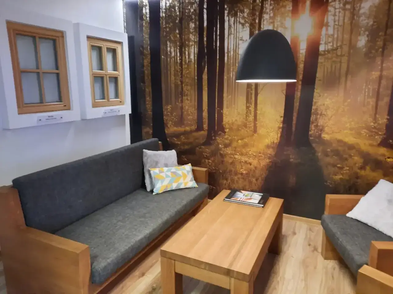 Salon z kanapą, stolikiem i oknami na tle leśnej tapety.
