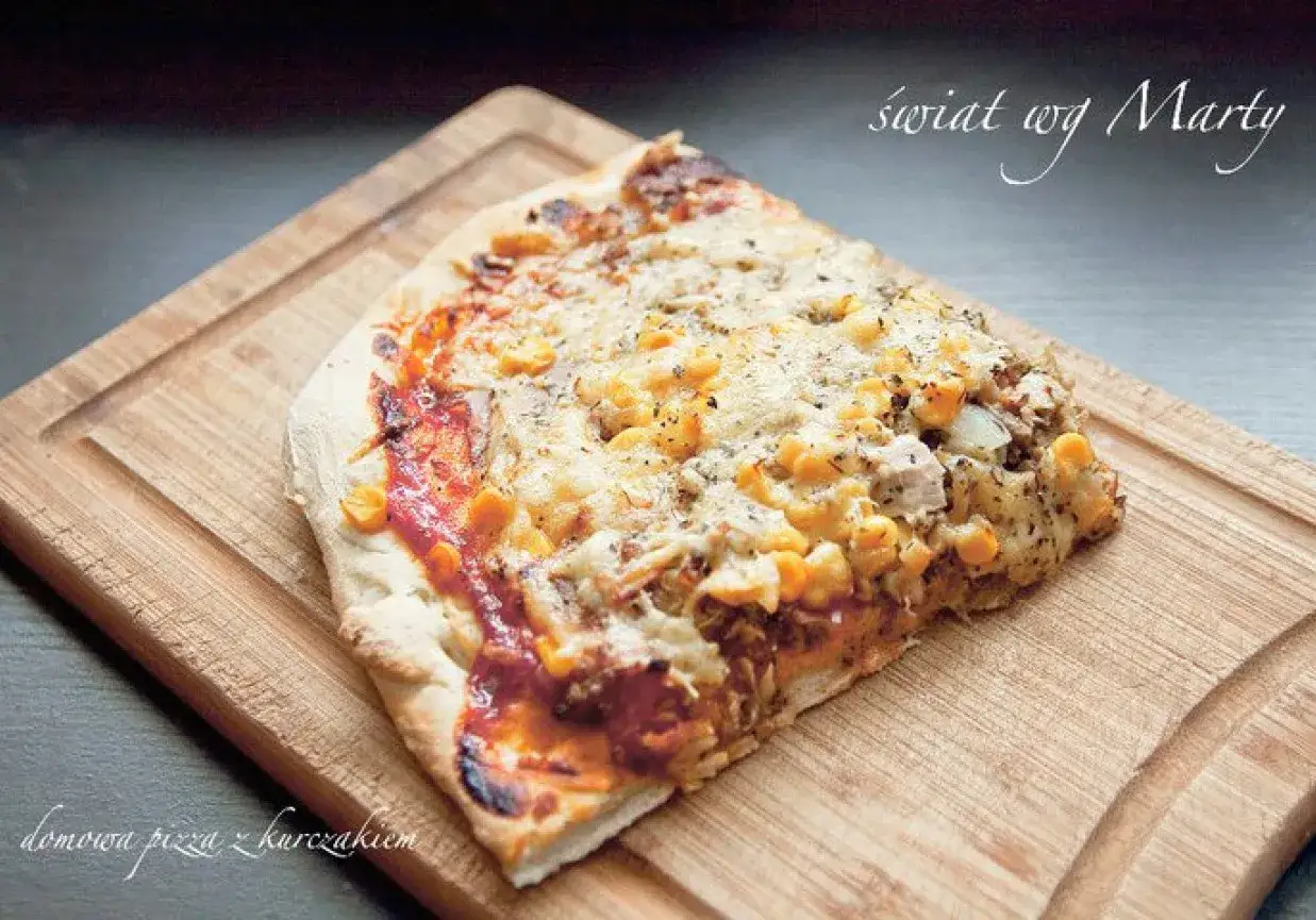 Domowa pizza z kurczakiem, kukurydzą i serem, podana na drewnianej desce.