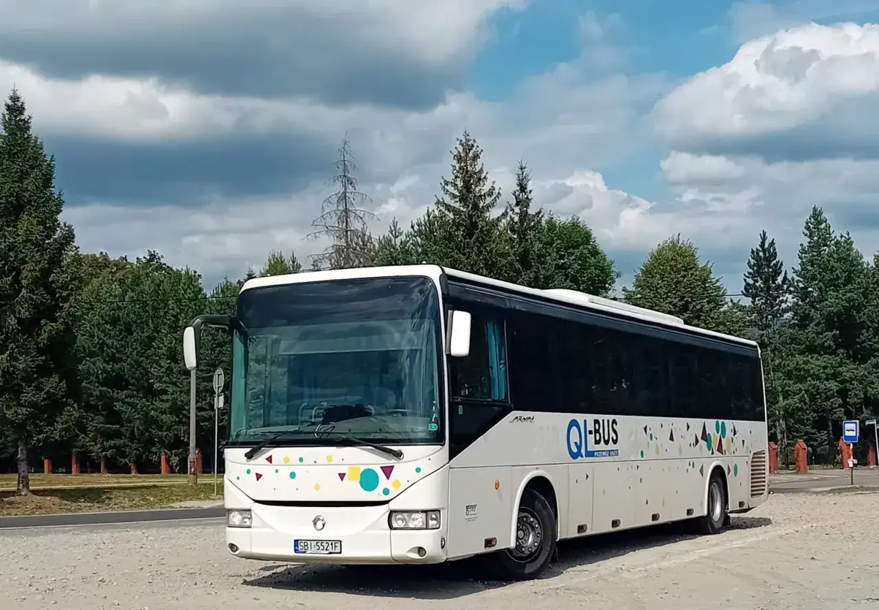 Biały bus z kolorowymi wzorami, gotowy do podróży. Kierowca z własnym busem, pewnie rusza w trasę.